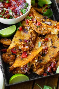 mexican food is served on a black tray with limes and cilantro sauce