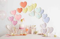 a table topped with lots of cakes and cupcakes next to a wall covered in paper hearts