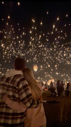 two people are looking at the sky full of balloons in the night with lights on them