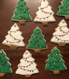 twelve decorated christmas tree cookies sitting on top of a wooden table