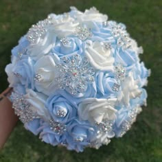 a bridal bouquet with blue and white flowers on the grass in front of someone's hand