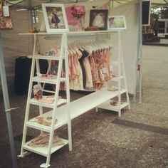 a white shelf under a tent with pictures and clothes hanging on the rack underneath it