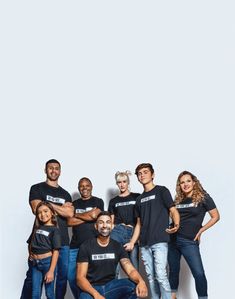 a group of people standing next to each other in front of a white wall wearing black t - shirts