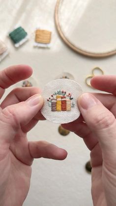 two hands holding up a small piece of fabric with some sewing supplies in the background