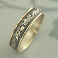 a gold and silver wedding ring with floral designs on the inside, sitting on a table