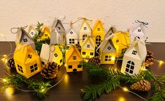 several small houses are decorated with pine cones and lights on the table next to evergreen branches