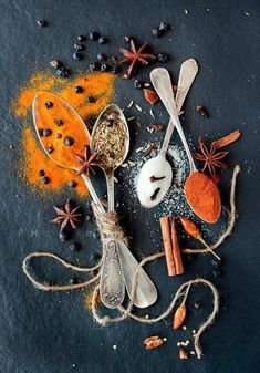 spices and spoons are arranged on a black surface