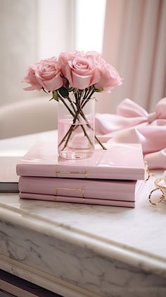 three pink roses in a vase on top of two books and a gold key sitting on a marble table