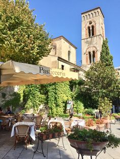 an outdoor restaurant with tables, chairs and umbrellas in front of a church tower