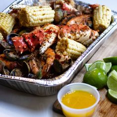 a pan filled with shrimp and corn on the cob next to lime wedges