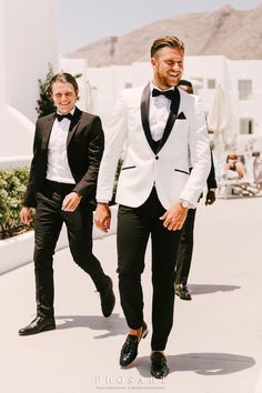 two men in tuxedos are walking down the street with one man wearing a black and white suit