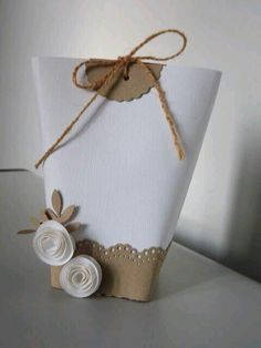 a small white box with some paper flowers on it's side and a brown string tied to the top