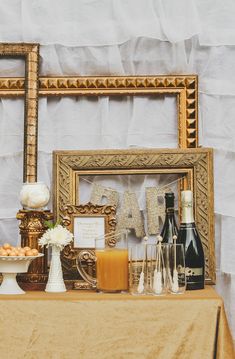 a table topped with bottles of wine and other items next to a gold framed sign