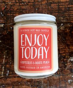 an orange and white candle with the words enjoy today on it sitting on a wooden surface