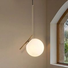 a modern light fixture hanging from the ceiling in a room with large windows and wood flooring