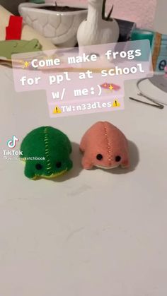 two small stuffed animals sitting next to each other on a white counter top in front of a sign that says, come make frogs for pt at school w / me