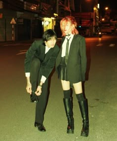 two people dressed in black and white posing for the camera at night with one holding his leg on the other's shoulder