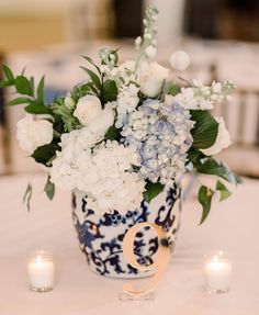 a vase filled with white and blue flowers on top of a table next to candles