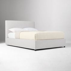 a bed with white sheets and pillows on top of it's headboard, in front of a gray wall