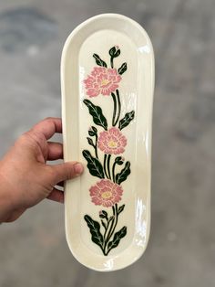 a hand holding up a white ceramic dish with flowers on the bottom and green leaves