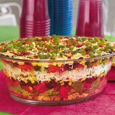 a large bowl filled with lots of food on top of a pink table cloth next to plastic cups