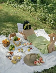 a woman in a green dress is laying on a blanket with food and drinks around her