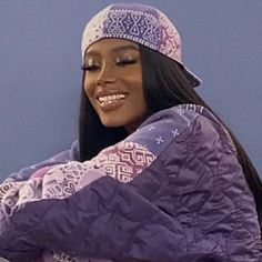 a woman wearing a purple jacket and hat with her arms folded over her head, smiling