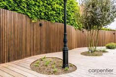 a lamp post in the middle of a wooden decked area with trees and bushes