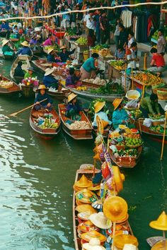 many boats are lined up on the water with people standing around them and selling goods