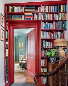 a red bookshelf filled with lots of books next to a chair and table