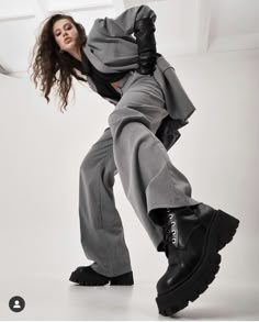 a woman in grey suit and black boots is posing for a photo with her hands on her hips