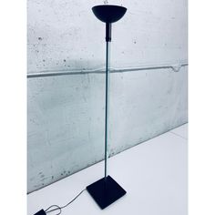 a black floor lamp on a white table next to a gray wall with a cord plugged into it