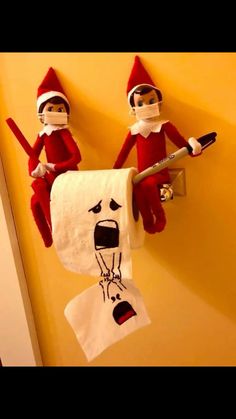 two elfs are hanging on the wall with toilet paper