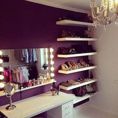 a room with a vanity, mirror and lights on the wall next to shelves filled with shoes