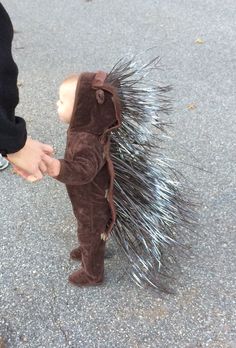 a small child holding an adult's hand while standing next to a toy porcupine