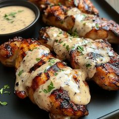 grilled chicken with sauce and garnishes on a black platter next to a small bowl of ranch dressing