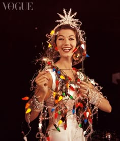 a woman in a white dress is smiling and holding some christmas lights on her head