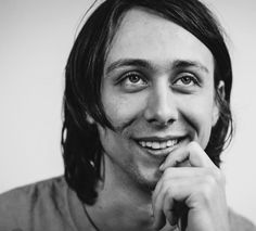 a black and white photo of a man with long hair smiling at the camera while wearing a t - shirt