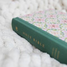 a green book laying on top of a white blanket next to a pink flowered pillow