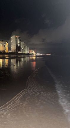 the city lights shine brightly in the dark sky over the water and beach at night