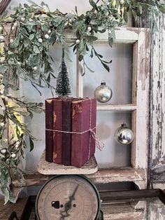 an old clock sitting on top of a table next to two books and a christmas tree