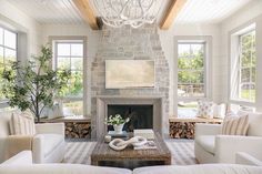 a living room filled with furniture and a fire place under a chandelier in front of two windows