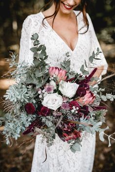 a woman holding a bouquet of flowers and greenery in her hands while smiling at the camera