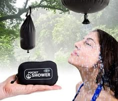 a woman is spraying water on her face with a shower head and black bag hanging from the tree