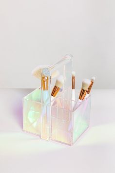 an assortment of makeup brushes in a clear holder on a white surface with light reflections