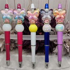 four different colored pens are lined up next to each other in front of some flowers