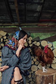 a woman sitting on top of a tree stump next to a chicken