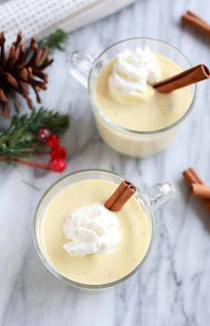 two mugs filled with whipped cream and cinnamon sticks on top of a marble table