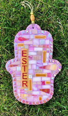 a hamsa hanging on the grass with words written in mosaic glass and gold foil