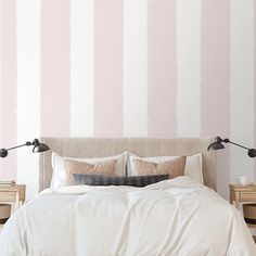 a bed with two lamps on each side and a pink striped wall in the background